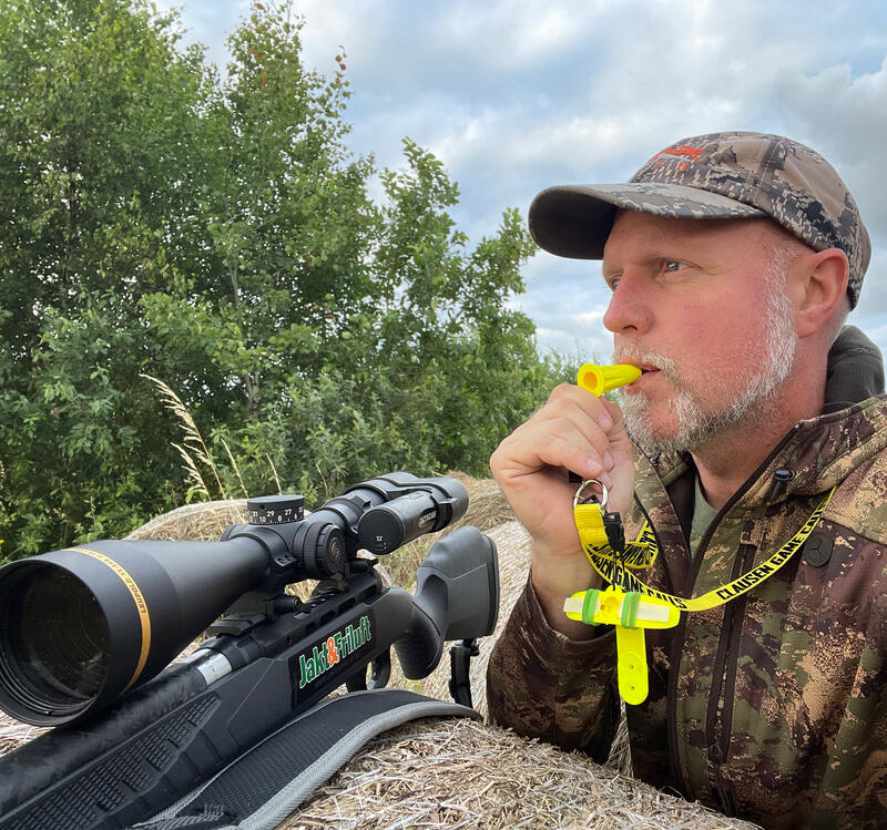 Mann med jaktvåpen sitter og blåser i lokkefløyte