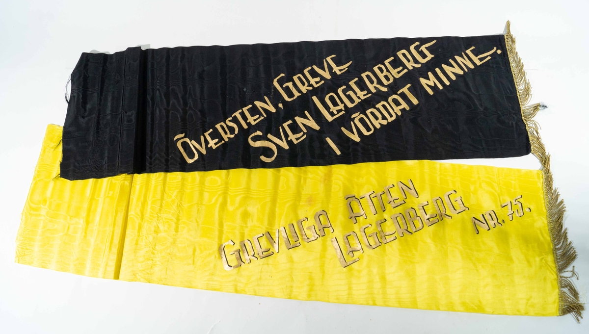 Svart band med guldfrans och text i guld: "Översten, greve Sven Lagerberg i vördat minne". Gult band med  guldfrans och text i guld: "Greveliga ätten Lagerberg Nr. 75."