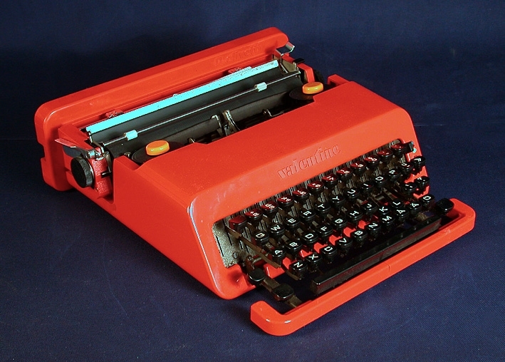 Skrivmaskin med hölje av klarröd plast, tillhörande fodral.
