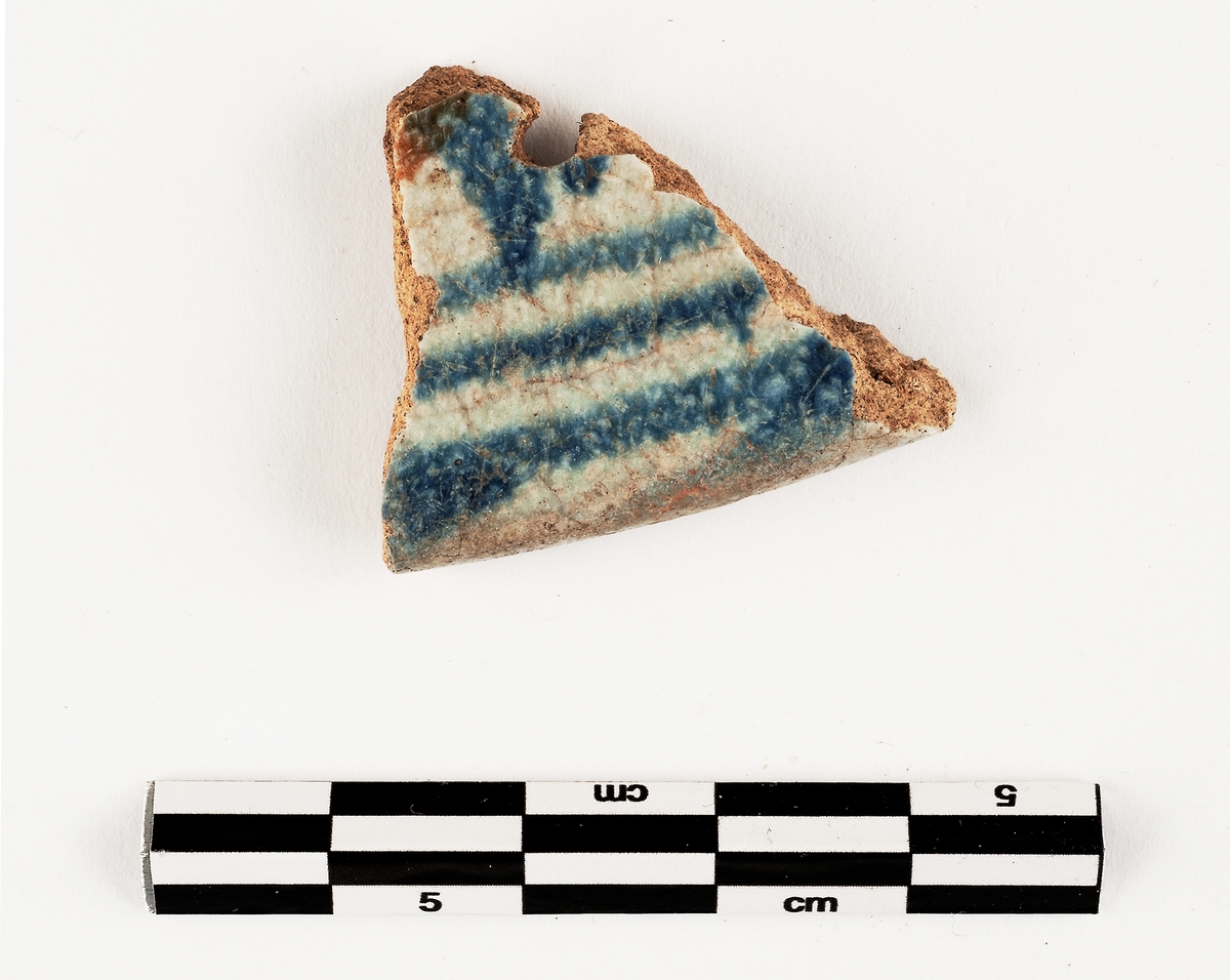 Del av kärl. Keramik. Fajans. Skål. Tennglaserad med blåvit dekor. Troligen holländsk import. Datering: 1580-1650.