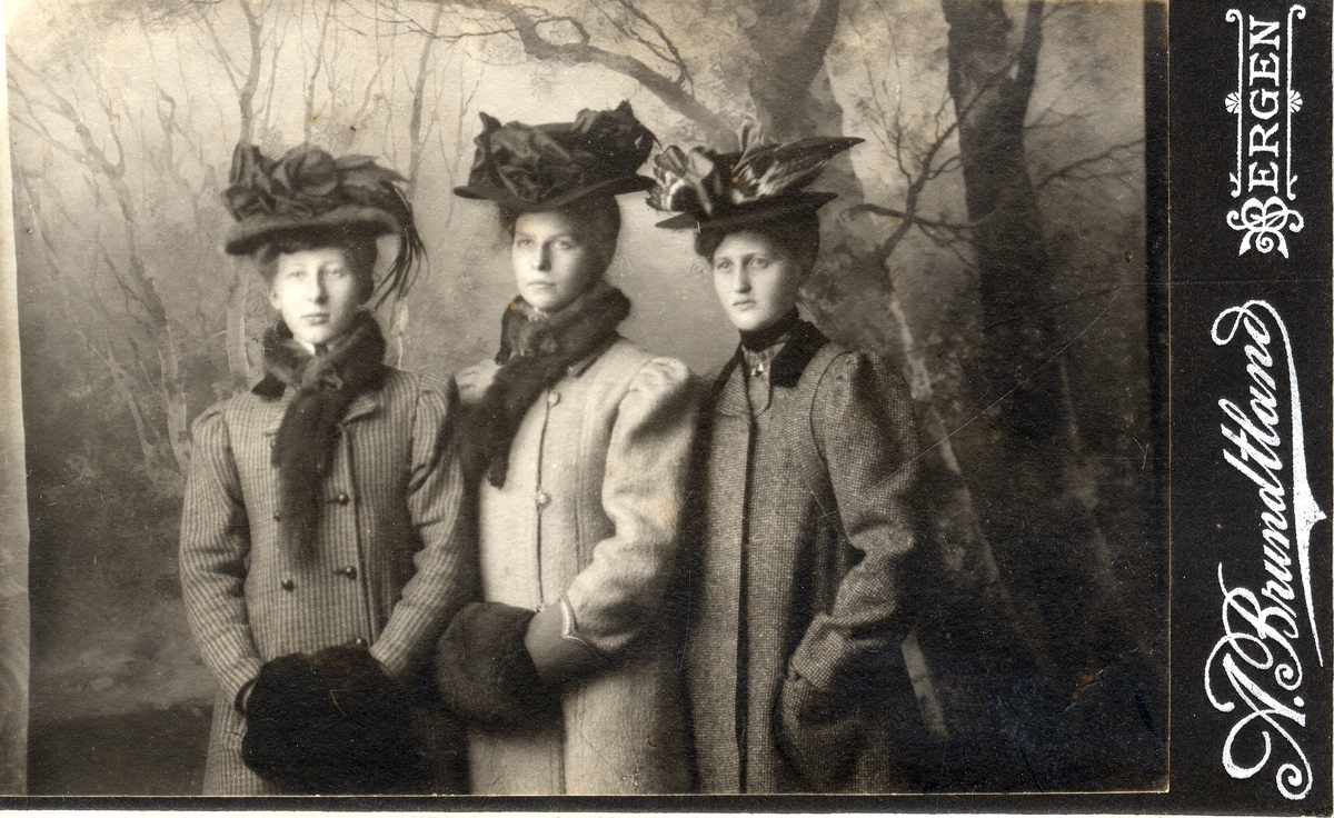 Studioportrett av tre kvinner i vinterkåper og hatter. Anna Andersen til venstre.