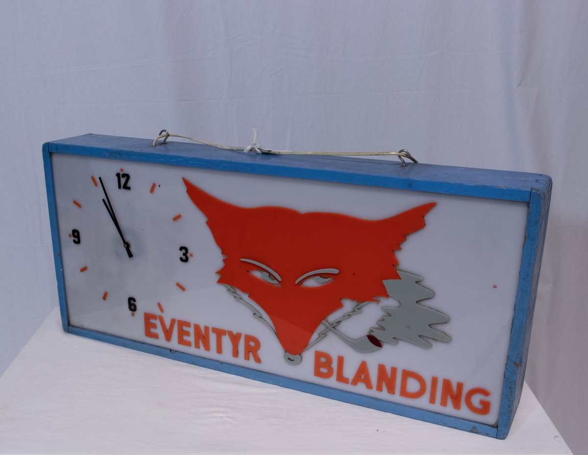 Rektangulært skilt med belysning. Viser en klokke, et rødt revehode og skriften "Eventyr Blanding"