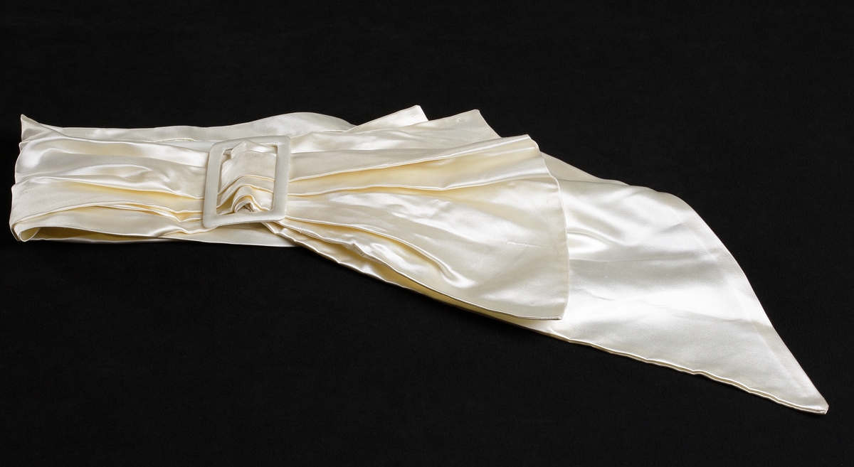 Sidenband att ha runt livet till brudklänning- Snedskuren, veckad, med en sölja i vit plast. Hela brudklänningen består av klänning, underkjol, jacka, skor, sidenband, handskar och brudkrona.