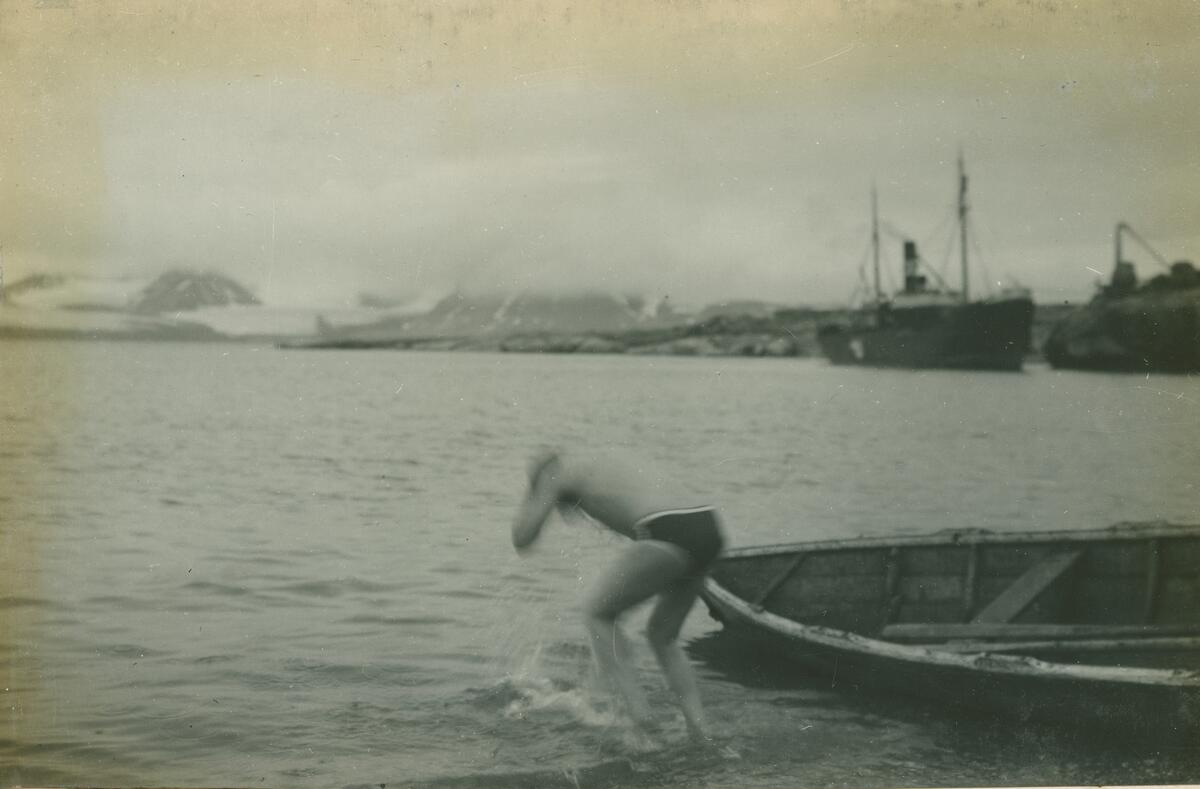 En mann bader seg i sjøen i Ny-London på Blomstrandhalvøya. Fraktebåten Activ i bakgrunn på kaia. Gjenstandsnummer SVB 2101