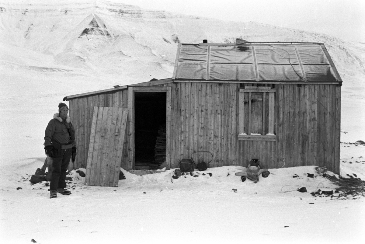En mann foran ei hytte.