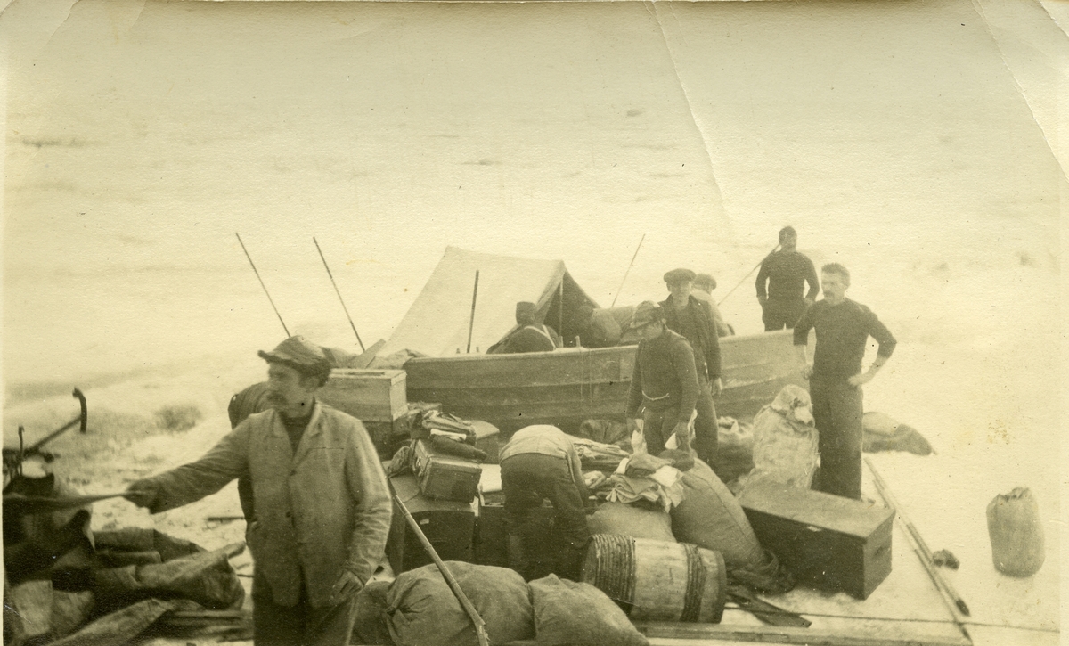 9 menn med en båt setter i land utstyr, tønner og mat et ukjent sted på Svalbard. Bilder fra Jens Kristoffer Bay sin bildesamling. Han var vinteren 1914/15 sjef for en overvintringsekspedisjon på Svalbard.