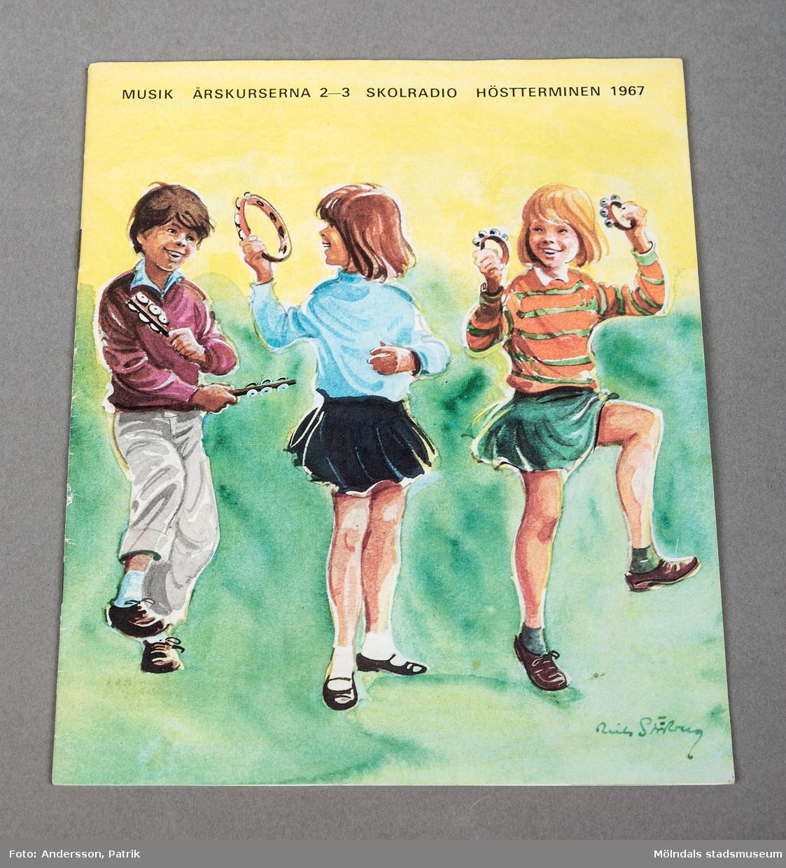 Ett mindre tunnt häfte. Framsidan är huvudsakligen gul och grön. Det finns en stor tecknad bild på tre skrattande barn i åtta-års åldern på framsidan. Det är en pojke och två flickor som håller rytminstrument i händerna. Barnen tar dansliknande steg i luften. Även baksidan föreställer tre barn spelande med instrument.