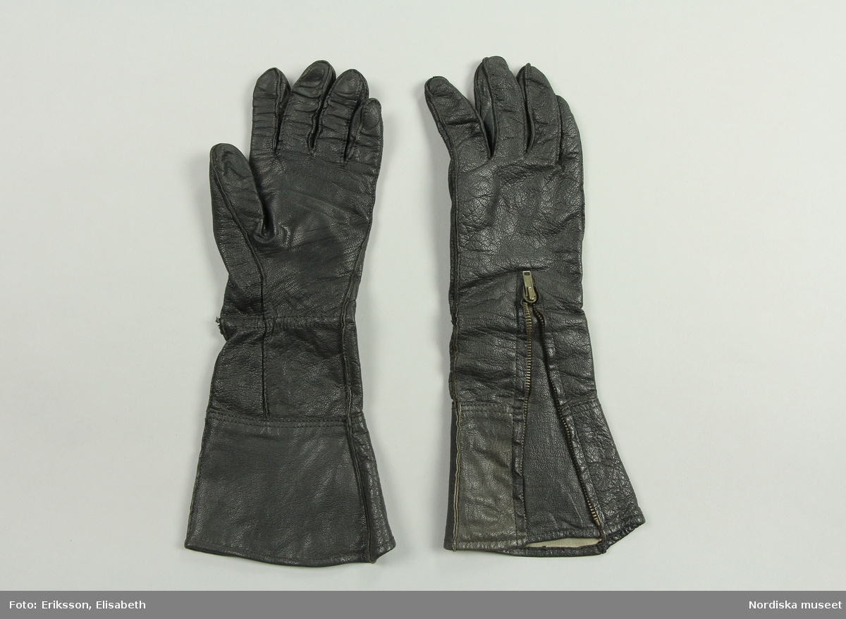 Motorcyckelhandskar (MC-handskar) svart läder med en metalldragkedja på oavansidan av handsken för att med dragkedjan kunna reglera handskens vidd på och avtagande.