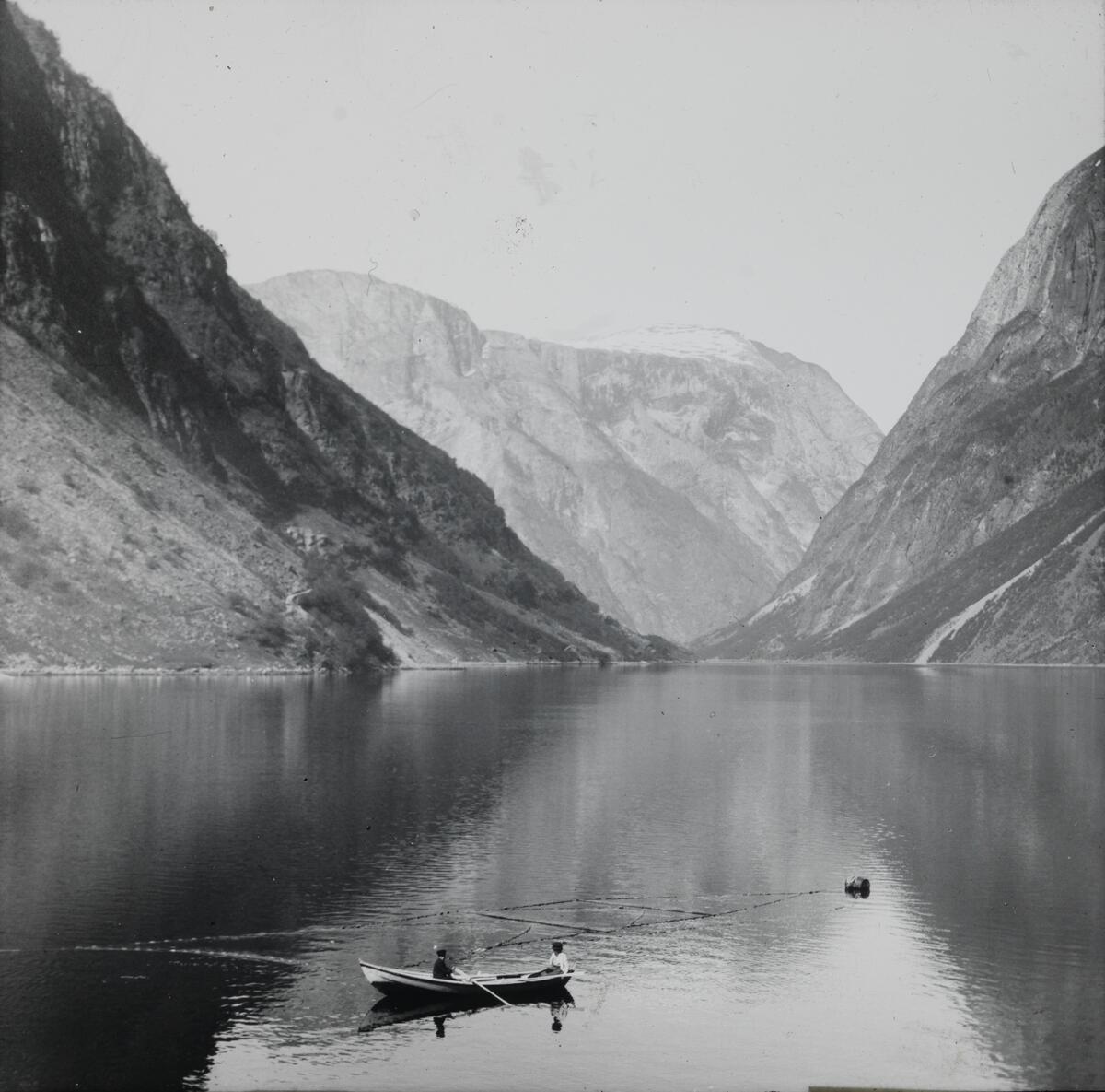 Dias. To personer ror ved et fiskeanlegg i Nærøfjorden.