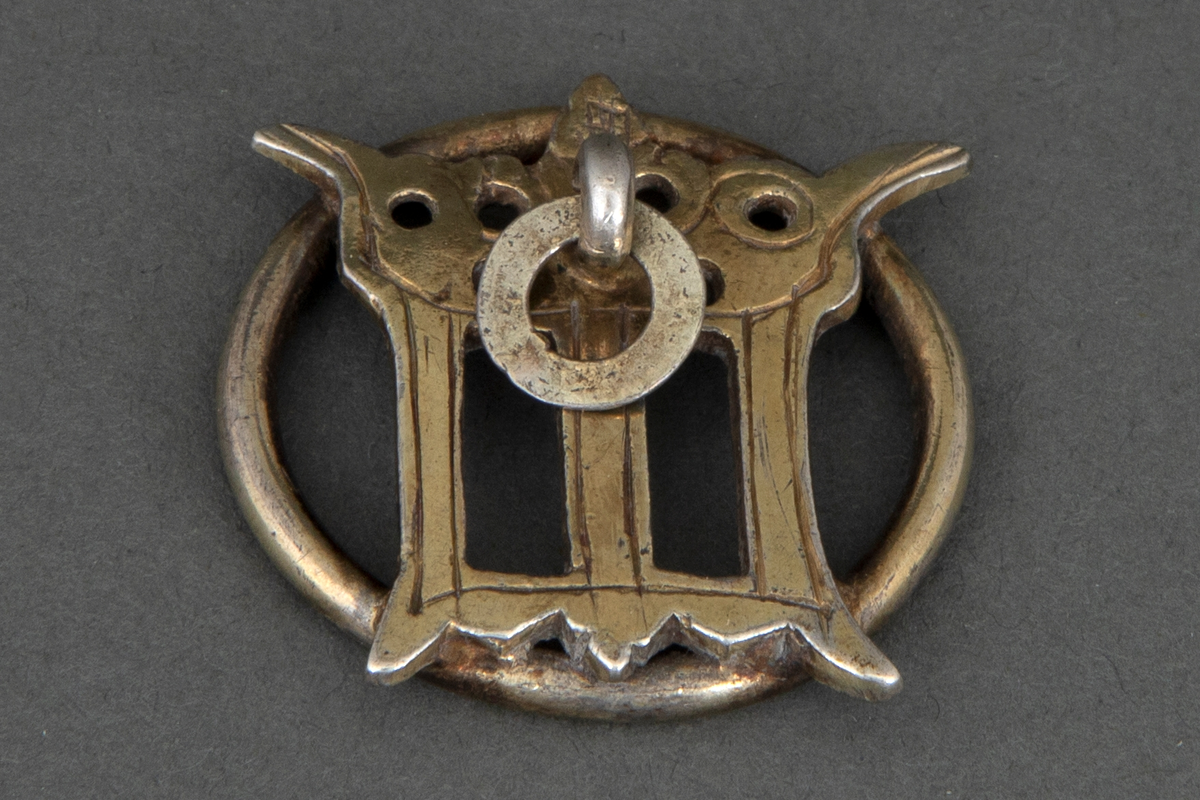Prydmalje i forgylt sølv. Kraftig ring med en påloddet gjennombrutt, og muligens, en sterkt stilisert utforming av kronet gotisk minuskel "m". Foran en bøyle med en nedhengende flat ring.