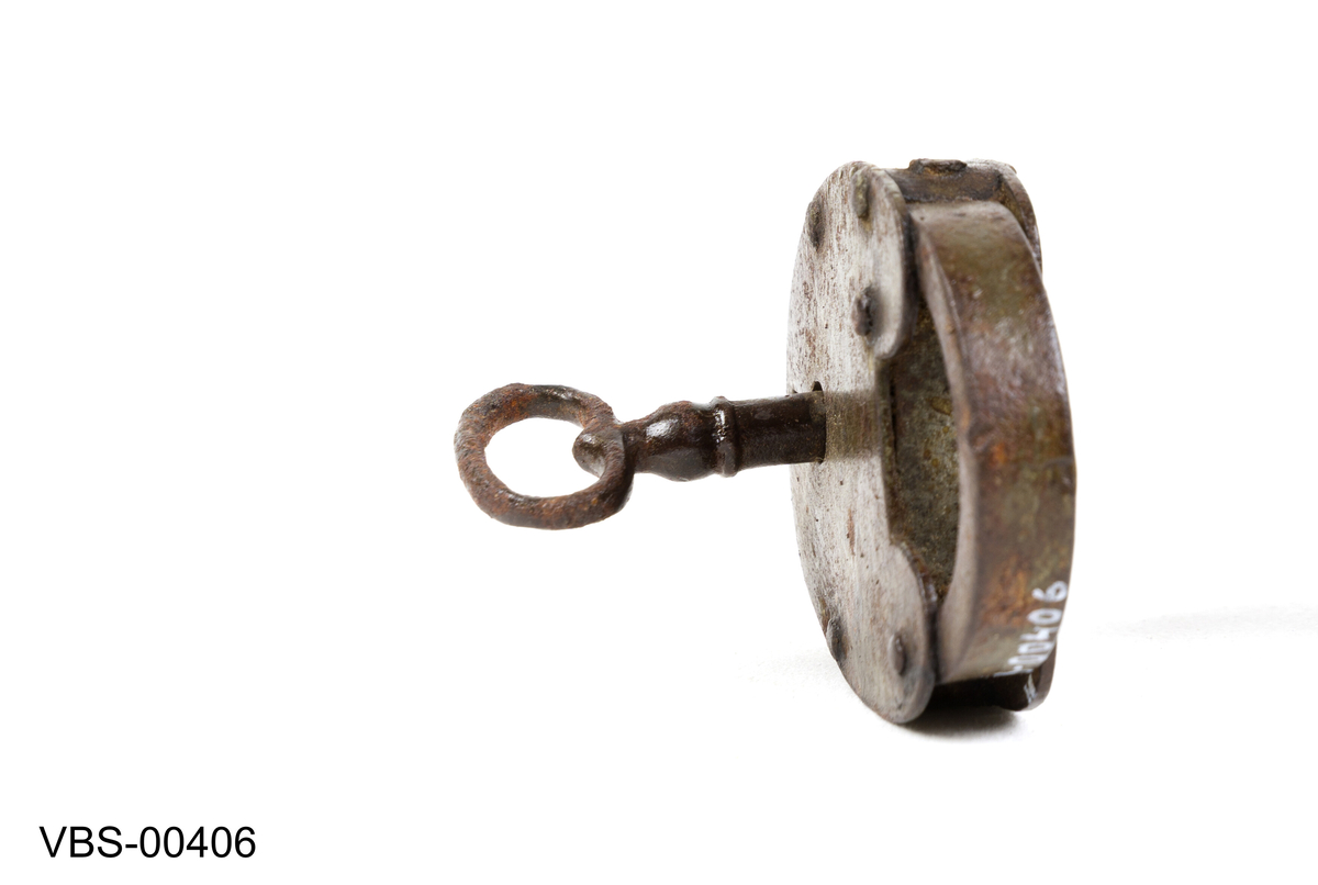 Oval, hjerteformet hengelås med nøkkel. 
Nøkkelen har rund bøyle, firkantet skjegg og hull pipe.