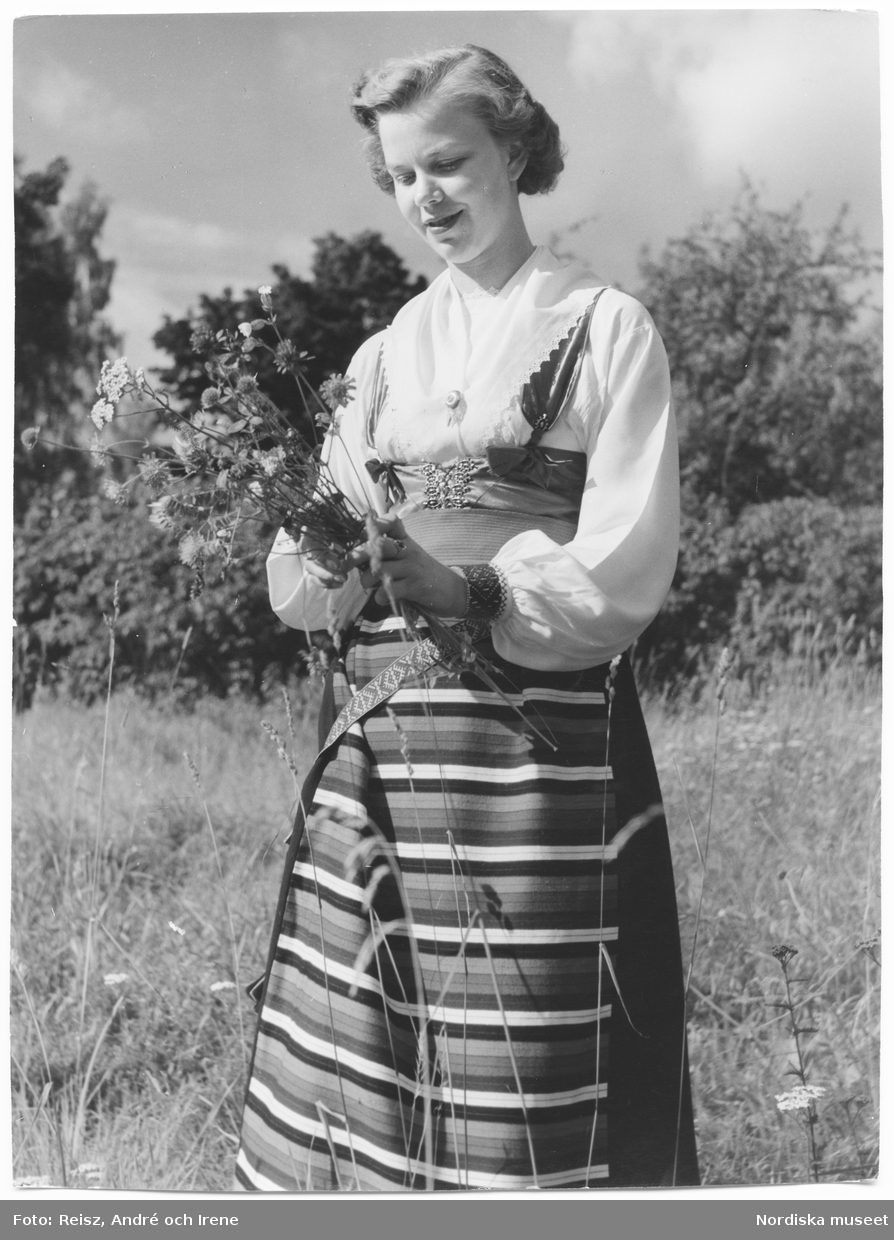 Dalarna. Porträtt av en ung kvinna i Rättviksdräkt med blommor i handen.