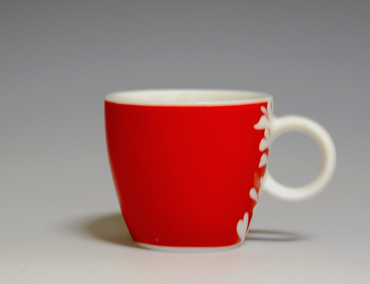 Espressokopp av porselen, med rund hank. Rød heldekkende dekor med utsparte blomster i hvitt.
Modell: Barista, forgitt av Poul Jensen.
Dekor: Red Kenya