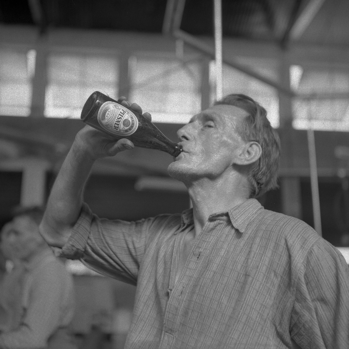 Foto av en man ur "degelgänget" som dricker en kall öl som belöning efter degelbytet. Se JEAK05062-JEAK05067