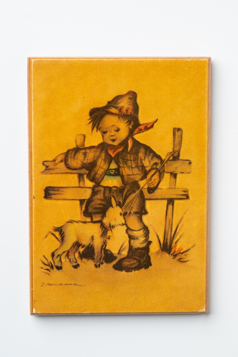 Prydnadstavla av trä med tryckt motiv av pojke och get vid ett staket. Pojken bär korta hängselbyxor och en toppig hatt. Färgsättningen är huvudsakligen brun, beige-gul med inslag av något röd och grön färg. Tavlan är lackad. På baksidan är handskrift med bläck : "Minne efter Gustav Lantz", och handskrivet med blyerts: "1:75". På baksidan finns borrhål för uppsättning på vägg.