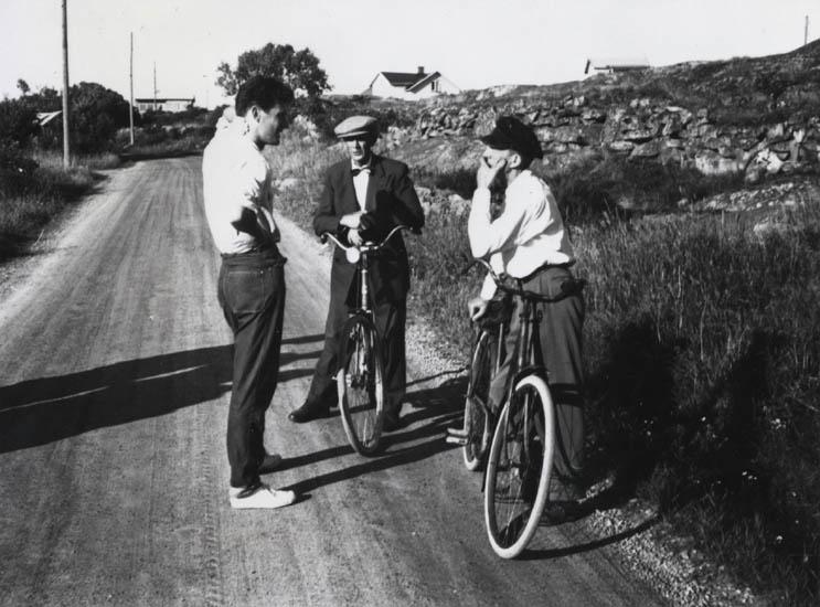 Tre unga män som står på en landsväg och pratar.