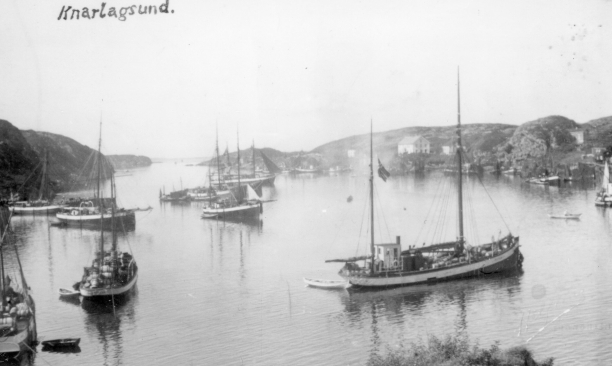 Prospektbilde : Knarlagsund i 1920-åra, havneområde med flere båter ankret opp. Bebyggelse og kystlandskap i bakgrunnen.