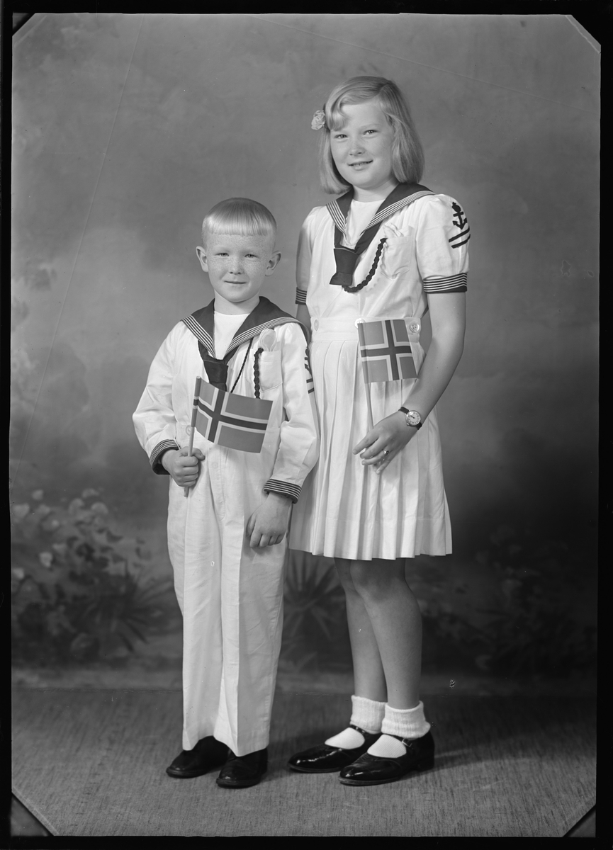 Portrett av to barn med finklær i matrosstil. Flagg i handa
