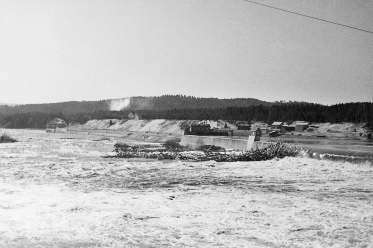 Tømmervase under dammen ved Skjefstadfossen i Glomma i Heradsbygda i Elverum, Hedmark, fotografert våren 1934. Dammen var 312 meter lang, og den skulle stuve opp vann til kraftstasjonen, som lå litt lengre nede, ved vestre elvebredd (til venstre for venstre bildekant her). Fotografiet ble tatt i 1. mai 1932, på et tidspunkt da elva var flomstor. Dette innebar at det gikk vann over hele damkrona, ikke bare den østre enden, som var litt lavere enn den vestre fordi man ønsket at mest mulig av fløtingstømmeret skulle gå i den østre delen av elveløpet, som var djupest. Dette fotografiet er tatt mot den vestre delen av dammen, der det var en 112 meter lang kanalmur som skulle lede driftsvann til kraftstasjonen gjennom ett, seinere to grove betongrør de 417 meterne ned mot kraftstasjonen, som skimtes helt til venstre i bildet. 

Skjefstadfossen hadde opprinnelig en fallhøyde på sju meter.  Ved bygginga av kraftverksdammen som dette fotografiet er tatt fra i 1909-1910 ble vannspeilet ovenfor Skjefstadfossen noe hevet, slik at fallhøyden ble økt til 10,5 meter.  Dette anlegget var det første store kraftverket som ble reist i den øvre delen av Glomma (nord for innsjøen Øyeren).