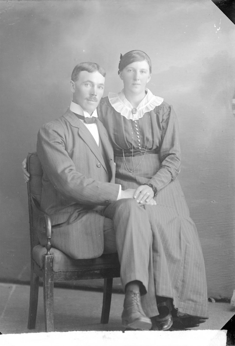Porträtt av en ung man och kvinna som sitter i en stol intill varandra och håller varandras hand.