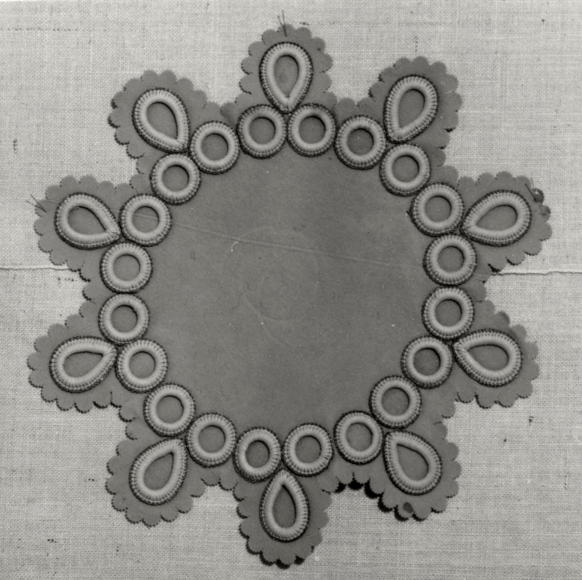 Duk, av ljust gråbrun filt, tio-uddig med runda och ovala snörmakerier med guldtrådskant, något defekt, malhål. Användningstid: 1880-1900