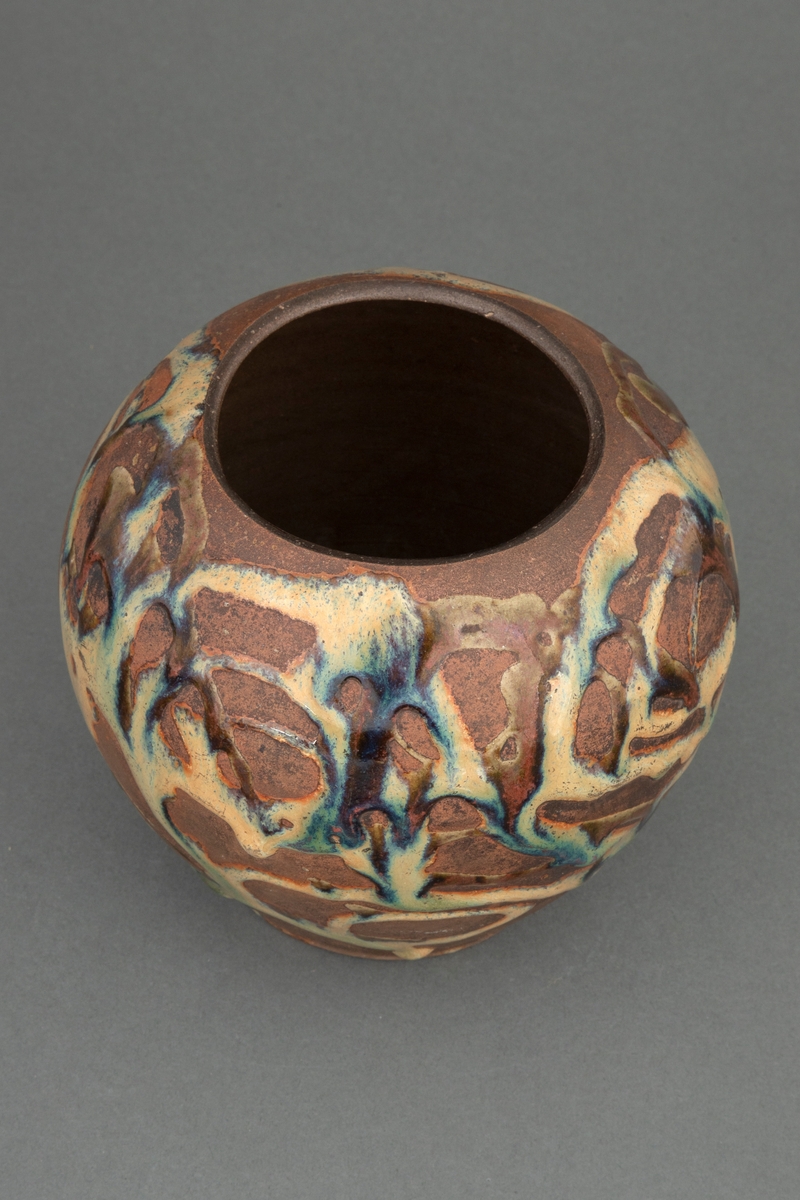 Kuleformet vase til bruk for blomster. smal åpning. Gråbrunt, hardt og tett gods. Utvendige årer av fritt flytende glasur, gulbrun, iblandet brunt og mørkeblått med metallisk skimmer.