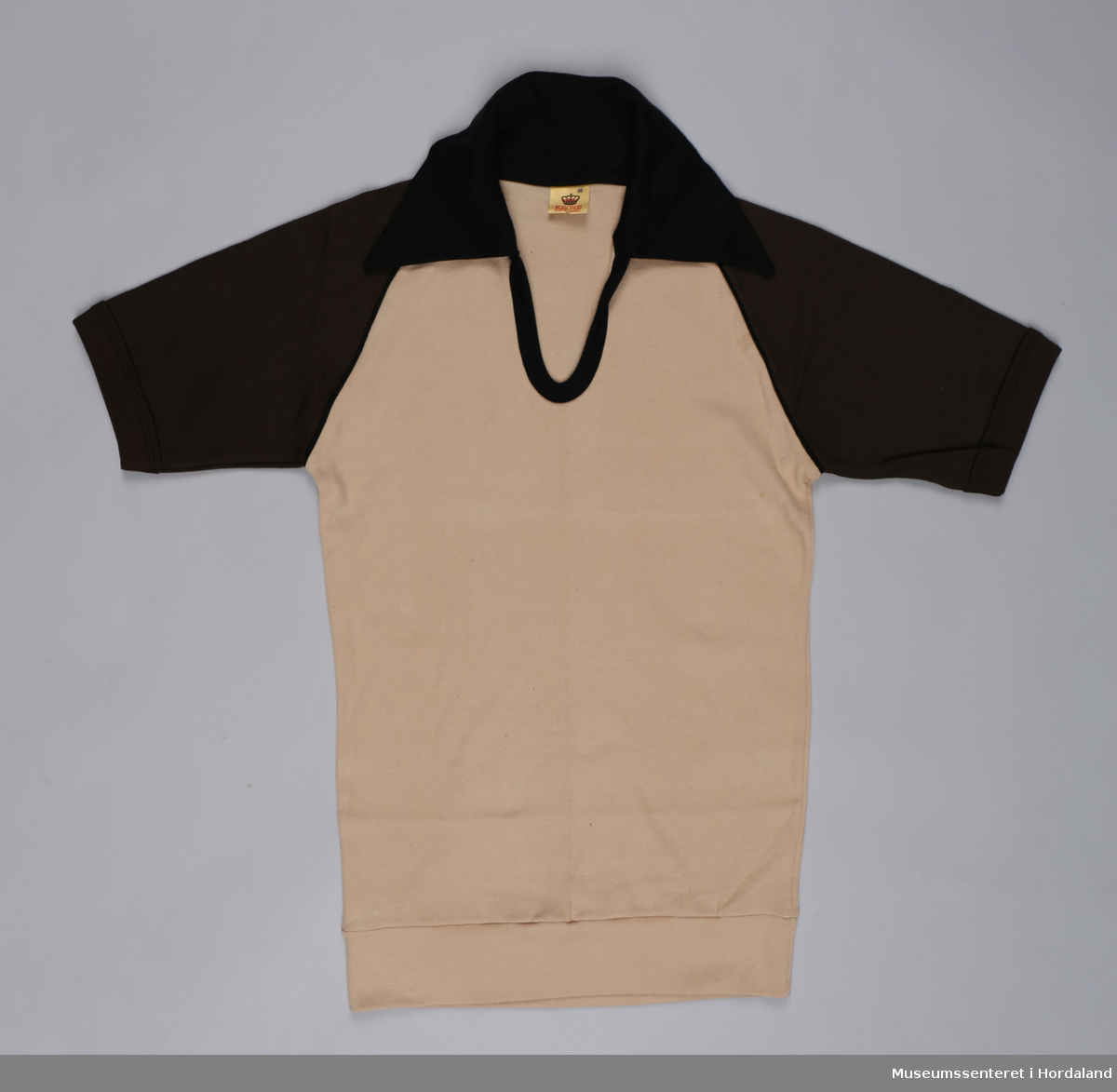 Beige t-skjorte i bomull med mørkebrune, korte erme, v-hals med svart kantavslutning og svart krage.