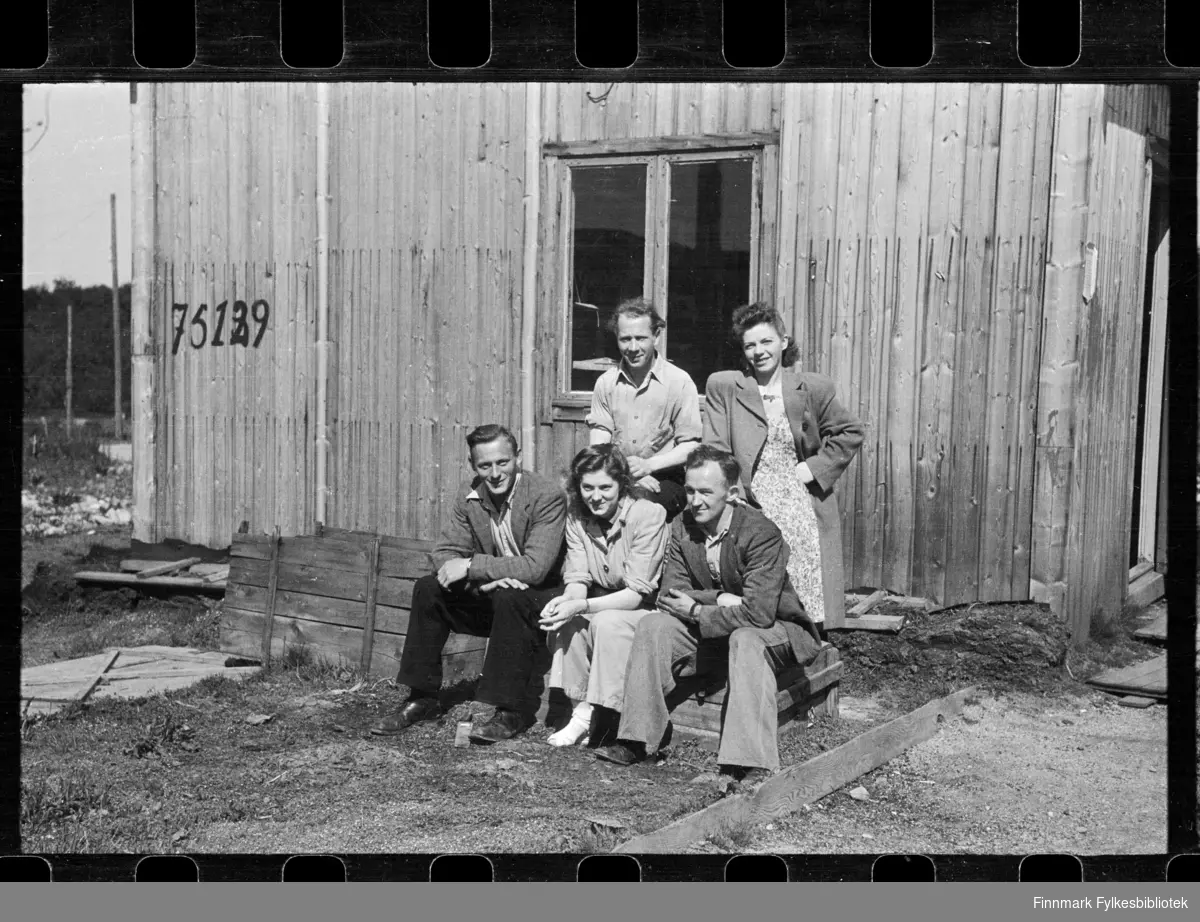 Foto av ukjent gruppe folk utenfor et hus med nummer 75129, antagelig i Kirkenes

Foto trolig tatt på slutten av 1940-tallet, eller tidlig 1950-tallet