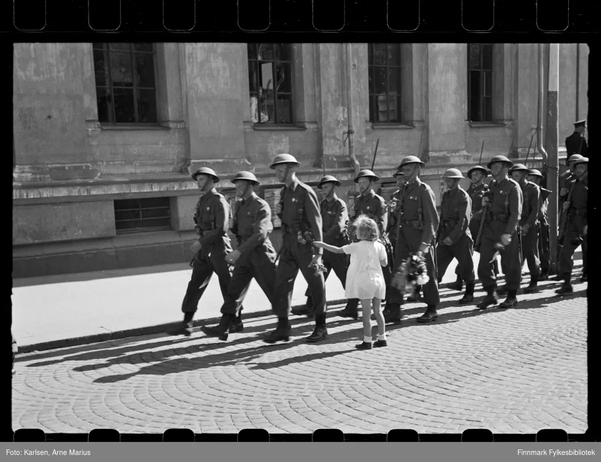 Britiske soldater marsjerer i parade i Oslo på de alliertes dag den 30. juni 1945 (The Allied Forces day)

Et barn har sprunget opp til soldatene for å rekke de blomster. Flere av soldatene bærer allerede på små buketter 
