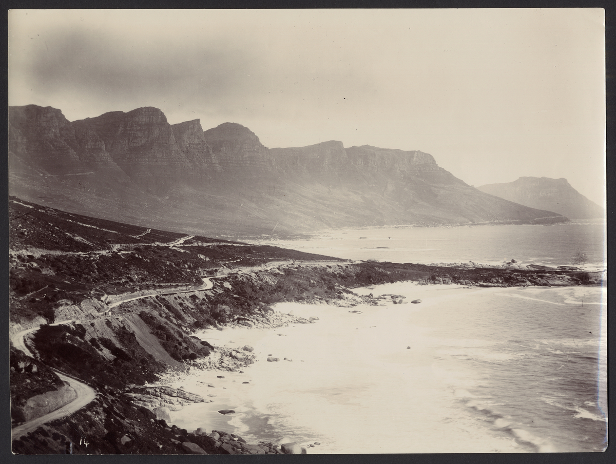 Bilden visar en kustväg i Sydafrika. Man ser höga bergsklippor till vänster sidan och havet till höger sidan.