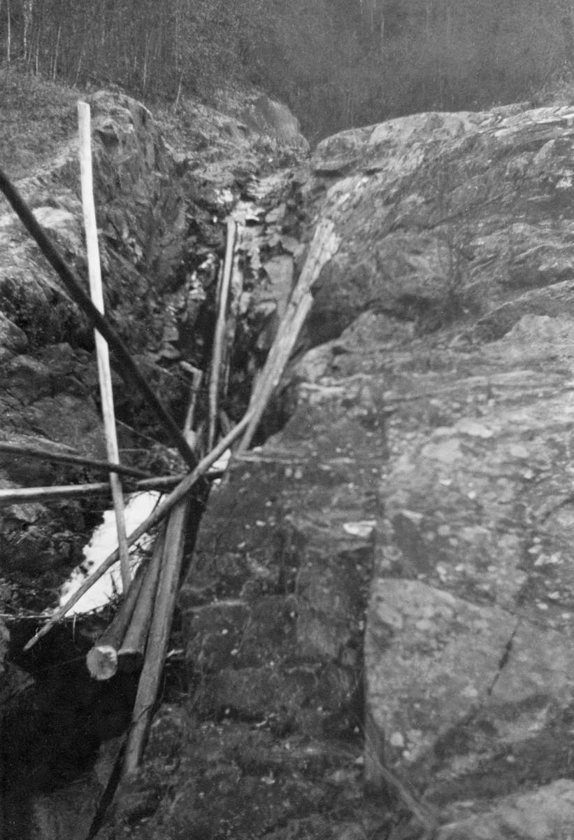 Bergspekk med tømmer, antakelig i en del av elva Leira på Romerike, der dette tømmeret har kilt seg fast og blitt liggende igjen etter at vårflommen var over.