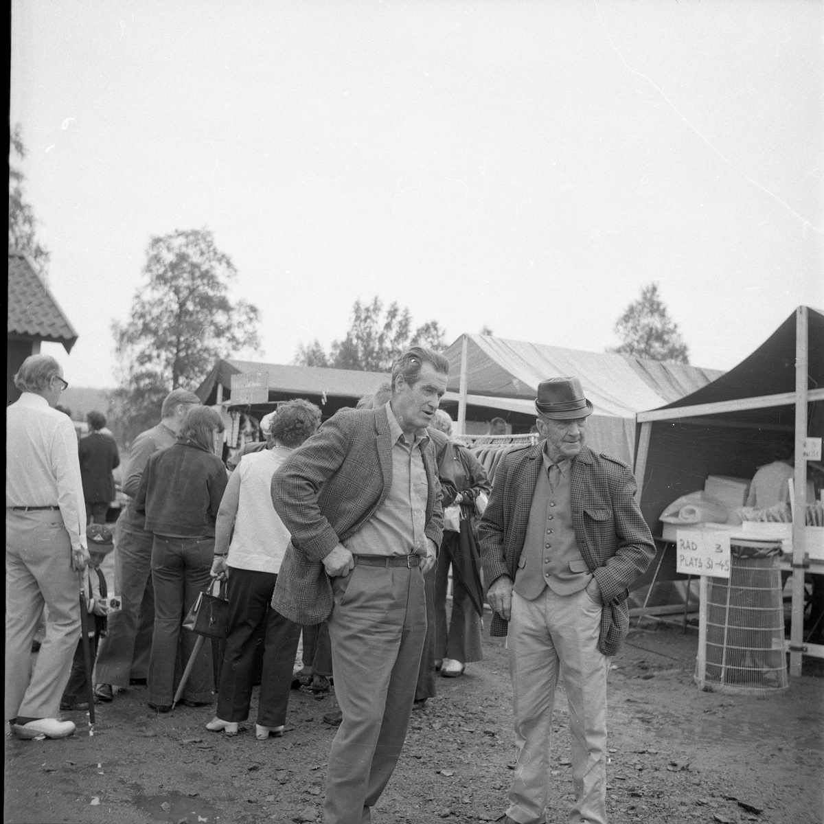 Folksamling på ett marknadsområde, två män i förgrunden.