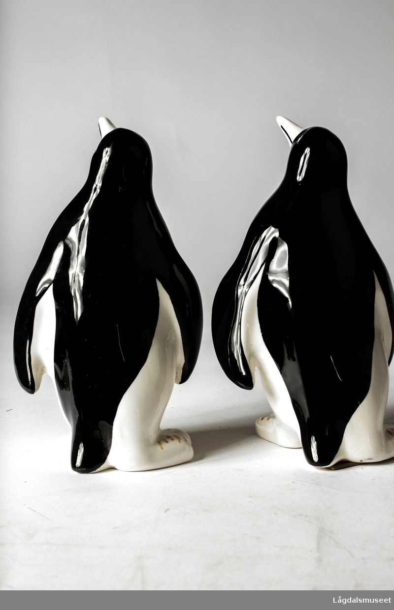Pingvin i fajanse med firmalogo for Jotun i hvite bokstaver på rødbrun bakgrunn på brystet til pingvinen.