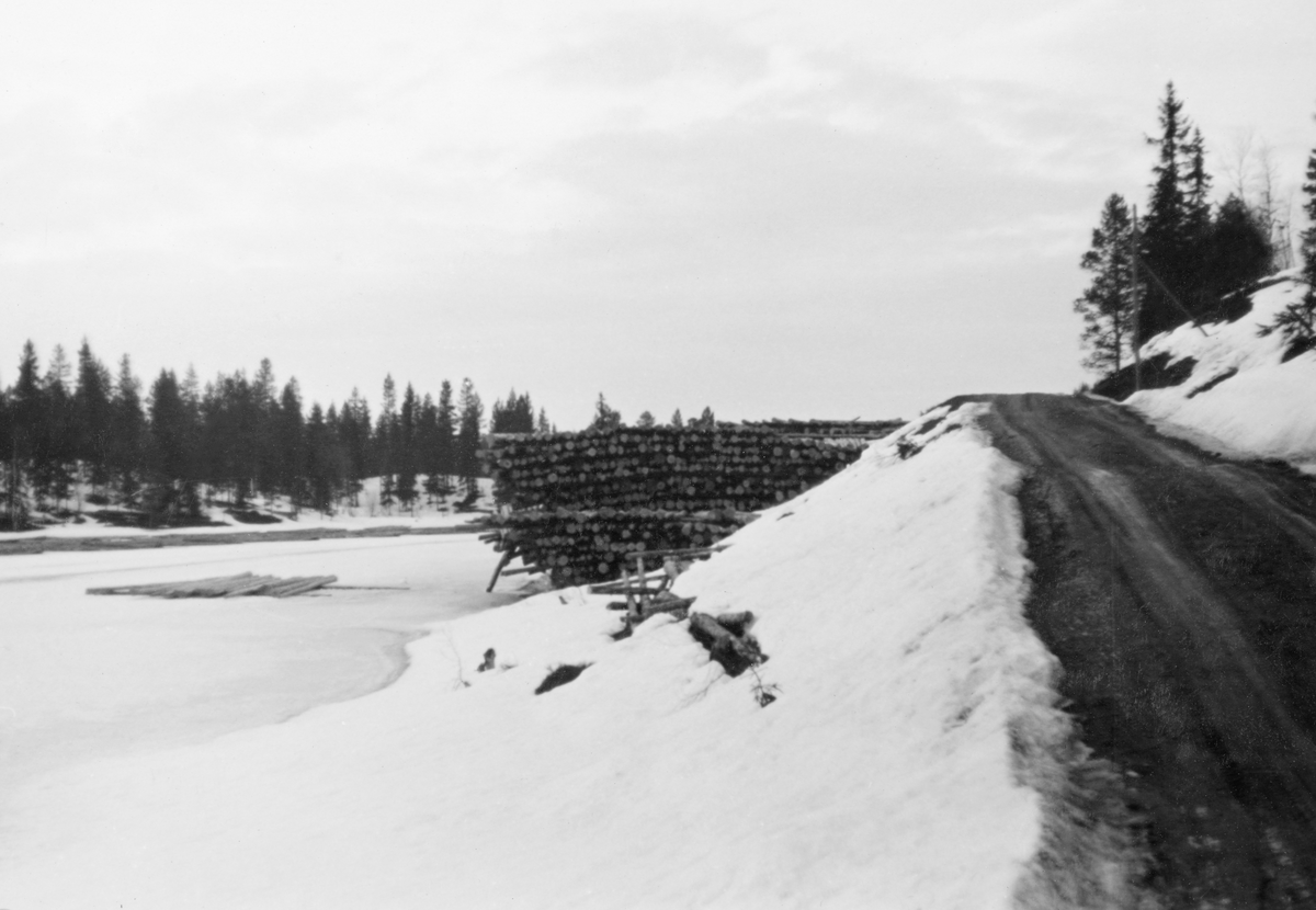 Tømmertillegging på Vesle-Osen i sørenden av Osensjøen, som ligger i Trysil kommune i Hedmark. Fotografiet er tatt vinteren 1938, og det viser to av de vanligste tilleggingsprinsippene for tømmer som skulle leveres ved fløtingsvassdrag når det gikk mot slutten av driftssesongen, altså på seinvinteren. Til venstre i bildet skimter vi ei snødekt isflate med såkalte flakvelter. Flakveltene besto av ett lag tømmerstokker som lå parallelt, men vinkelrett på to underlagsstokker. Underlagsstokkene skulle forebygge at tømmeret frøs ned i is og ble altfor fuktmettete etter eventuelle perioder med overvann. Fordelen ved denne tilleggingsmåten var at tømmeret ble veldig lett tilgjengelig for måling og merking. Her var det lett å se og kvalitetsvurdere hver enkelt stokk, med påfølgende «klaving» (diametermåling) og påslåing av kjøpermerker. Stokkene i flakveltene skulle ligge med de lengdemålene skogsarbeiderne hadde hogd på med romertall under apteringa oppovervendt, for å lette målernes arbeid. For å være noenlunde sikker på at tømmeret ikke ble altfor nedsnødd og nediset skulle det helst ikke legges tømmer i flakvelter for tidlig på vinteren. På elvebrinken til høyre ser vi ei såkalt strøvelte. I strøveltene var det flere lag (flak eller floer) med tømmer som var lagt oppå hverandre for å oppnå god tørk før fløtingssesongen. Tømmeret i floene lå alltid parallelt med strandlinja eller elvebredden, slik at det var en overkommelig sak å rulle stokkene uti vannet når fløtinga skulle starte. Denne tilleggingsmåten minimerte faren for at fløtingsvirket skulle bli for vannmettet og synke på sin veg nedover vassdraget.