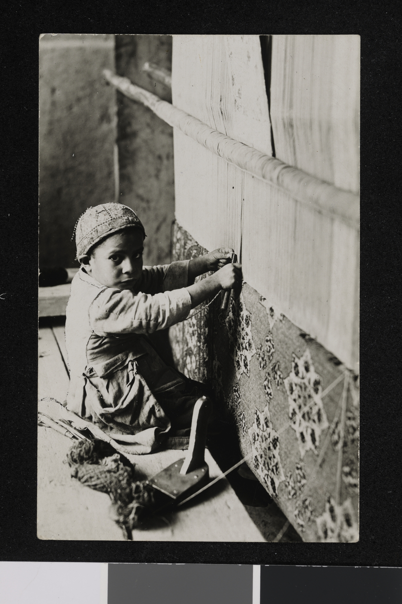 Portrett av en gutt ved siden av en teppevev. Fotografi tatt/samlet i forbindelse med Elisabeth Meyers bok; En Kvinnes ferd til Persia.