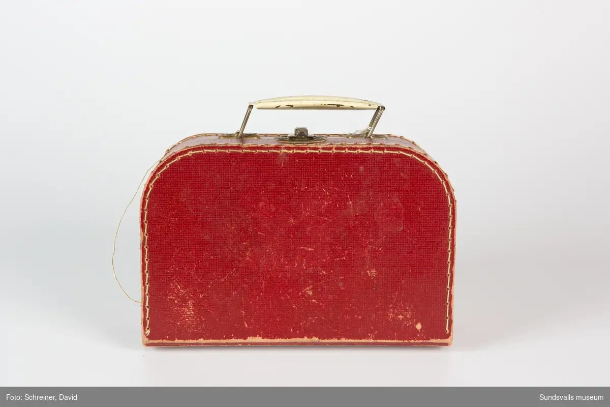 Röd frisörväska av papp som ihopfogats med hjälp av metallnitar och tråd. Handtag och låsanordning av metall. Handtaget är vitmålat.