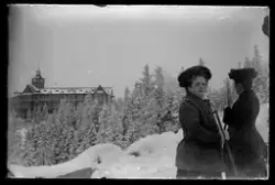 To damer utendørs om vinteren med en stor bygning i bakgrunn