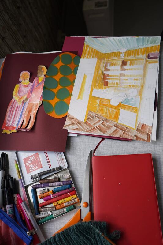 Bildet viser er arbeidsbord med malingstuber, tegnesaker og et uferdig maleri på papir