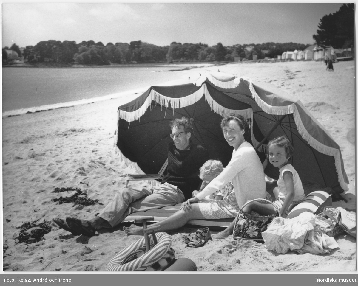 Familj som sitter på stranden under parasoll.