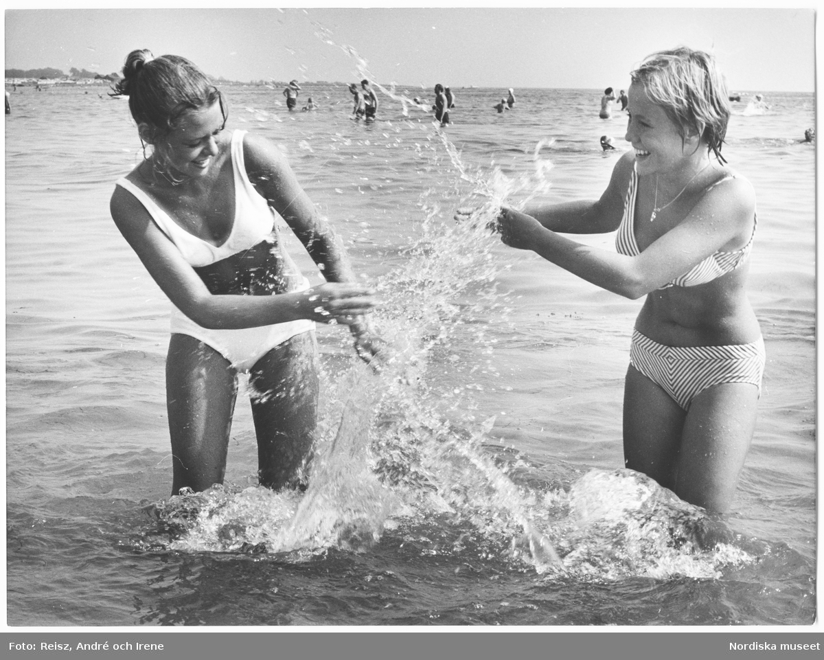 Två unga kvinnor skvätter havsvatten på varandra.
