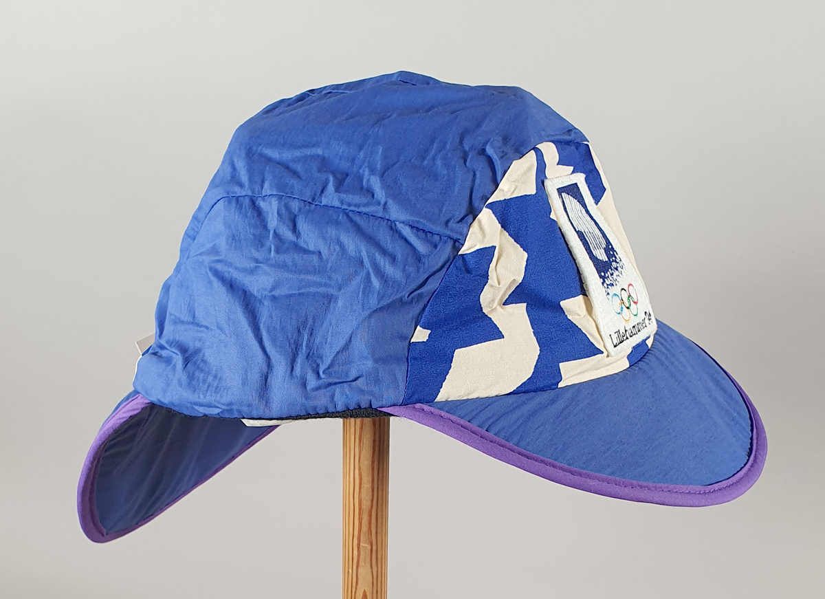 Blå caps med krystallmønster i hvitt. Skygge foran og bak, med snor som kan strammes bak. Tekstilmerke med emblem for Lillehammer '94 foran.