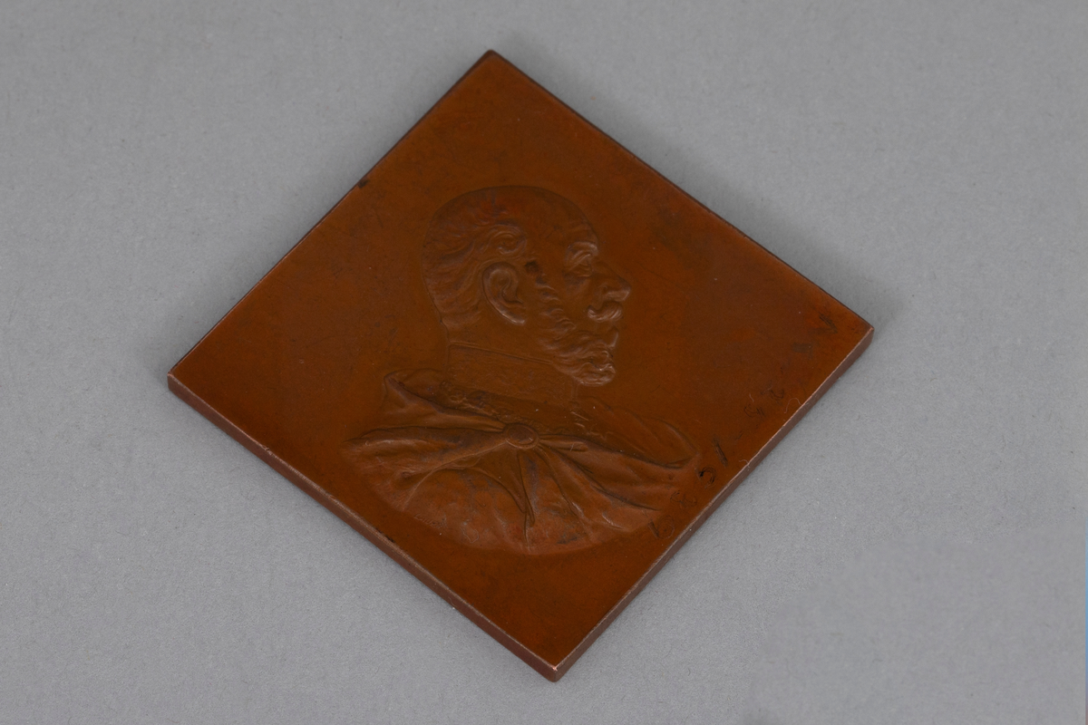 Kvadratisk medalje i bronse med punslet dekor. På avers er det fremstilt et mannshode i profil. På revers ørnevåpen og tekst.