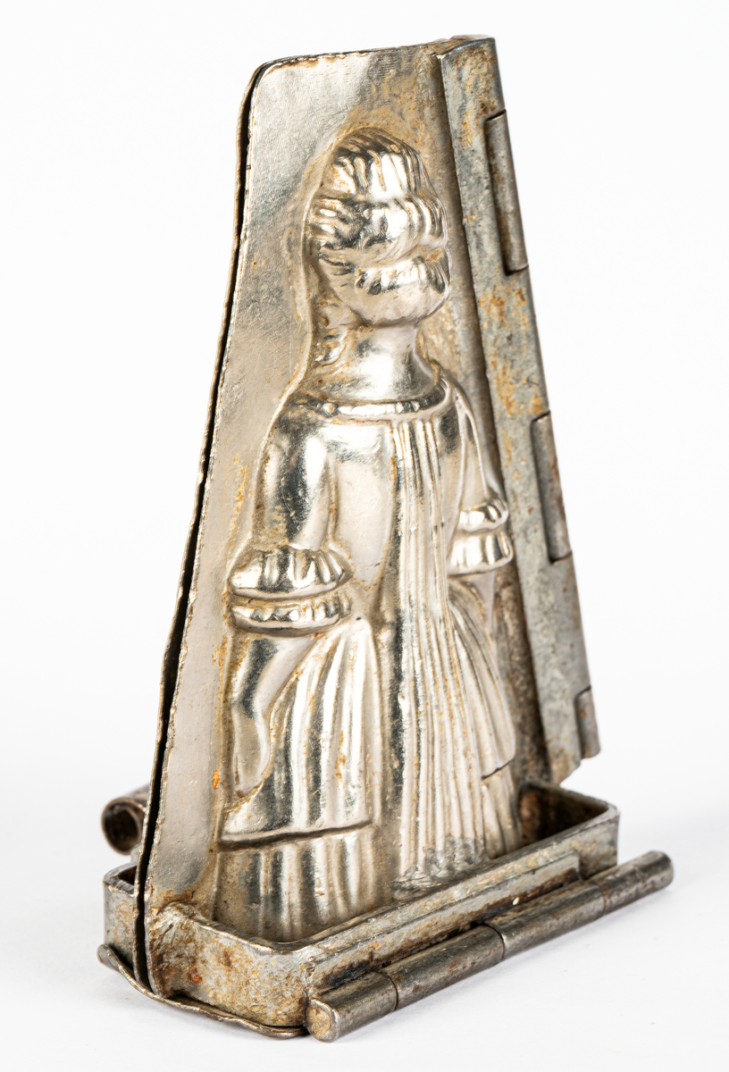 Gjutform i nickel, för choklad, föreställande en kvinna i 1700-talsklänning. Gångjärn i sidan på formen. Tillverkad av Henri Le Cerf i Köln, Tyskland.