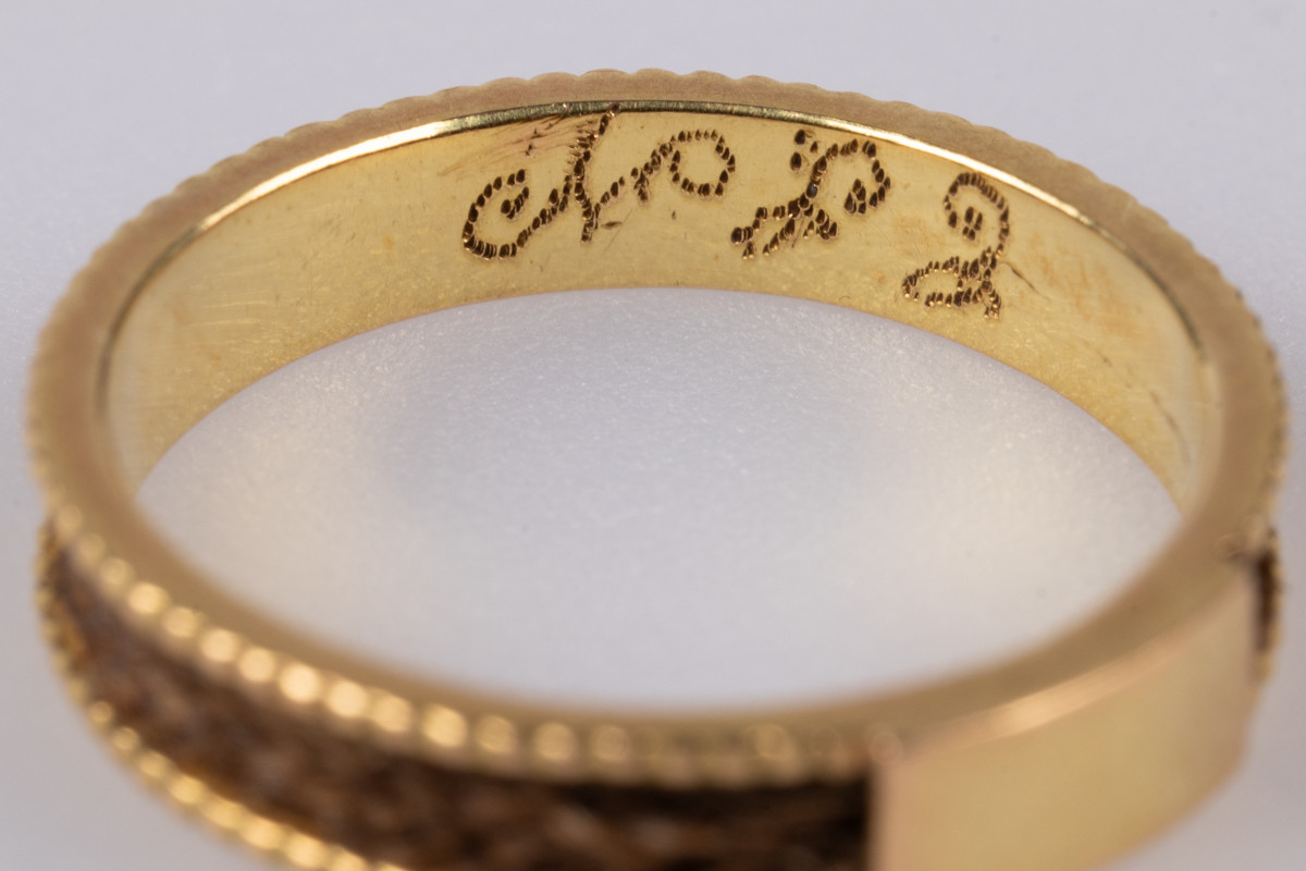 18 karats gullring med flettet hår rundt yttersiden av ringen. På innsiden er der et legeringsstempel og inngravert monogram