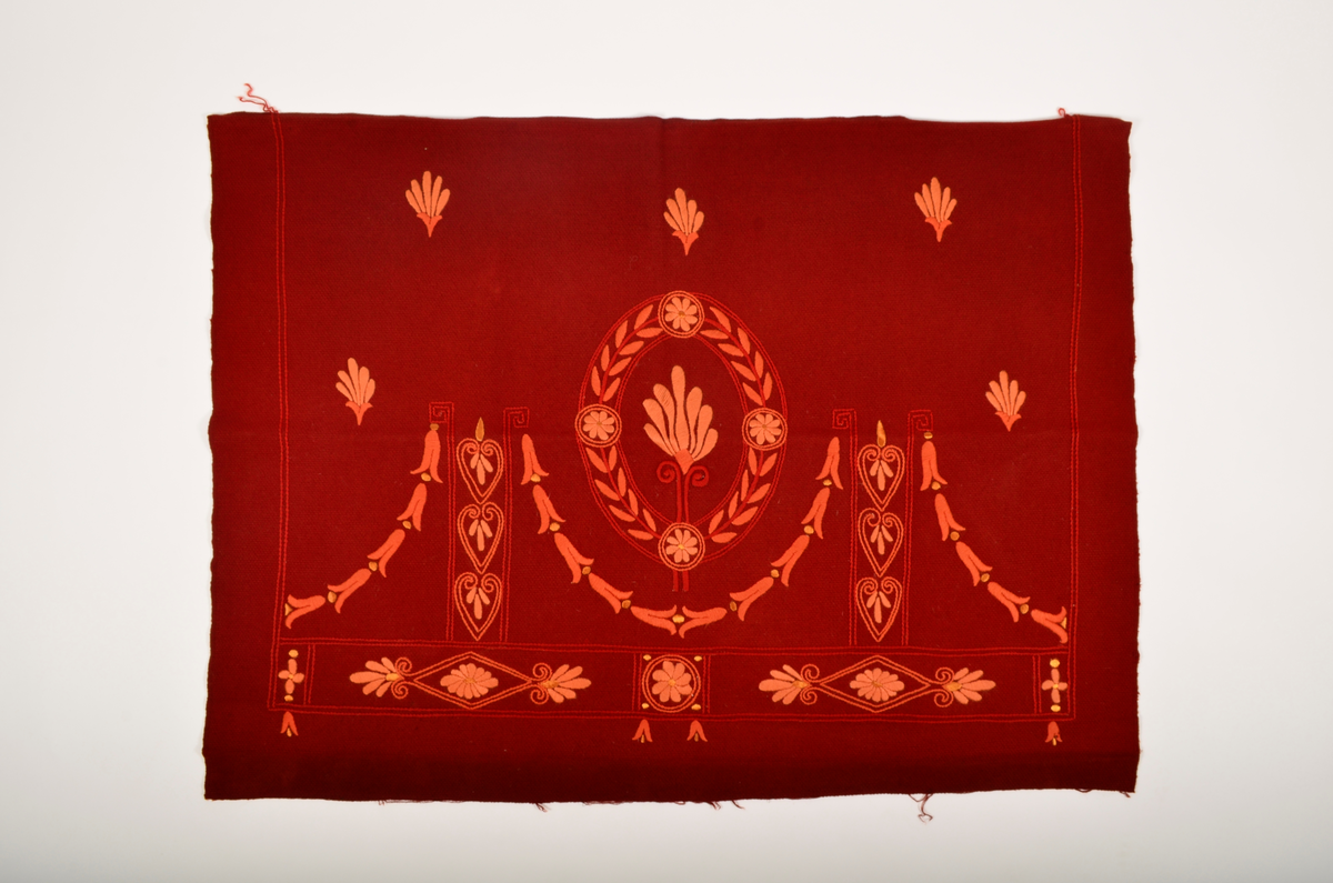 Rødt tekstil dekorert med broderi i ulike rød og oransje farger.