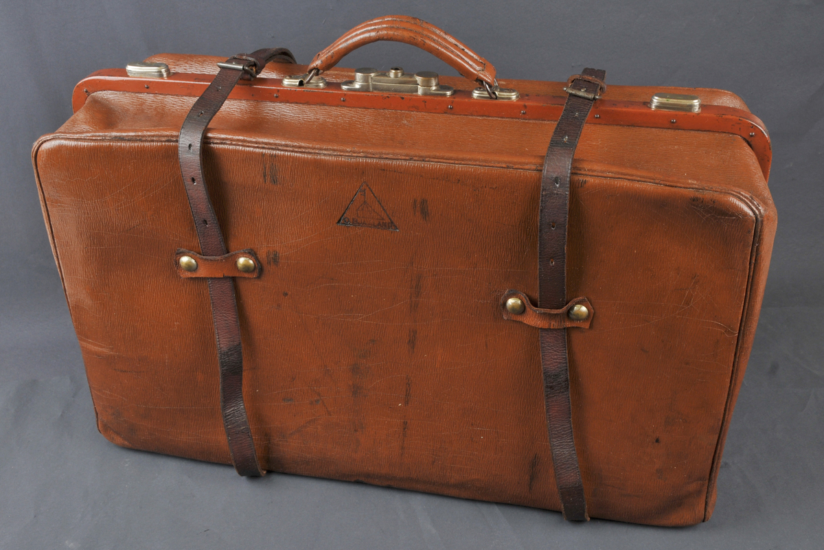 Laga av brunt skinn. 2 sprettereimar rundt
kufferten, metallås på midten med ein metallhake på låsen, lærhandtak. Innkomen frå O.Bjaaland.