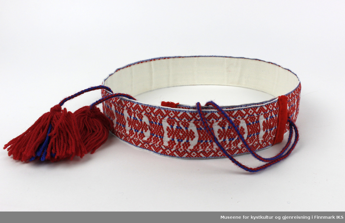 Et samisk belte vevd av ull og bomull. Belte har flettet bånd med dusker, og beltespenne slika at belte kan reguleres i lengde. På innsiden av belte er det påsydd lerret som gir belte en avstivet form.    

Belte er dekorert med et geometrisk mønster i rødt og blått. Mønsteret brukes i Karasjok, Porsanger, Utsjok og Tana dalen.