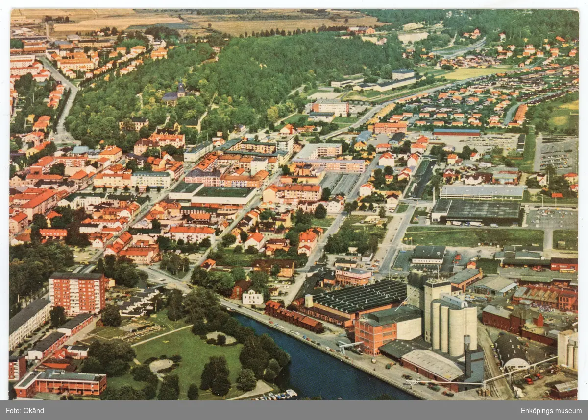 Vykort med flygfoto över centrala Enköping. Längs ned ser vi ån och hamnen. Fotograferat någon gång i mitten av 1970- talet. På kortet står det att försvarsstaben har godkänt fotograferingen den 12/5- 1974.