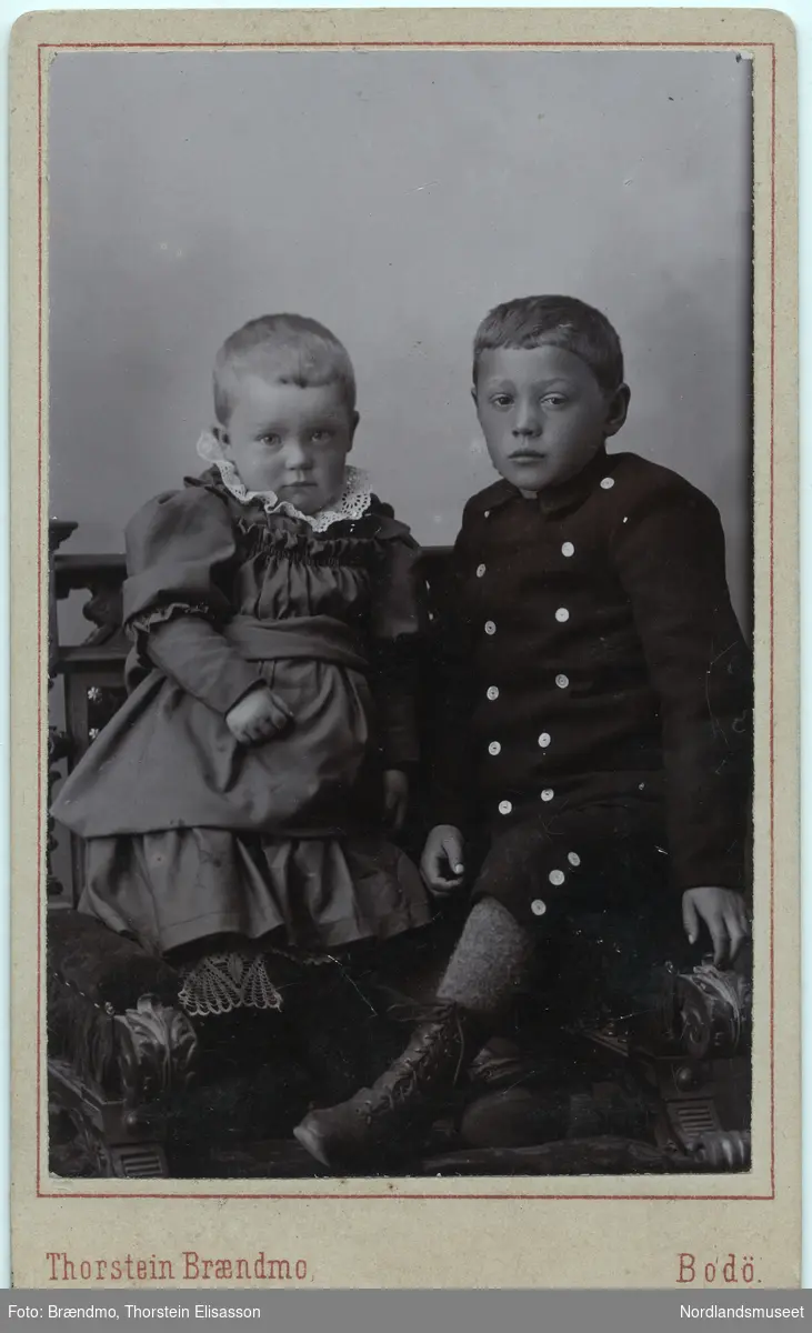 Portrettbilde av en liten jente i kjole og en noen år eldre gutt i korte bukser. Gerda Marie Fremmerlid og Kristoffer Ellingsen. Atelierbilde.