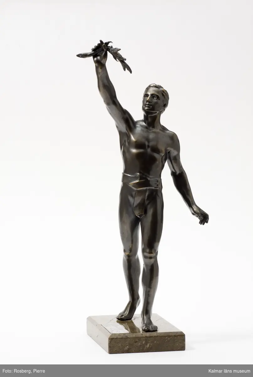KLM 15376:5. Statyett, av brons och sten. Mansfigur med lagerkvist i uppsträckt hand. Textplatta: 2:a pris Eksjö runt 1925.